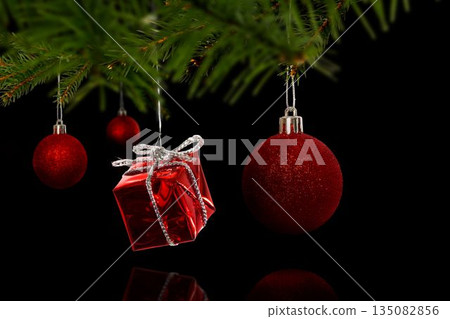 Cluster of red ornaments is hanging from green pine branch in 3D render with black background 135082856