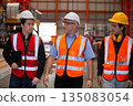 Three industrial engineers wearing safety uniform walk and discuss operations inside heavy factory, representing leadership, teamwork, and communication in high-risk industrial. 135083054