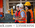 Three industrial engineers wearing safety uniform walk and discuss operations inside heavy factory, representing leadership, teamwork, and communication in high-risk industrial. 135083056