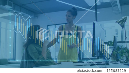 Discussing coworkers in yellow overalls at open-plan office with smartphone and barchart overlay 135083229