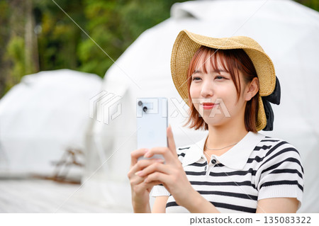 A woman taking a photo with her smartphone in front of the dome tent (Photo courtesy of Oki Seaside Resort Miyabi) A woman taking a photo with her smartphone in front of the dome tent (Photo courtesy of Oki Seaside Resort Miyabi) 135083322