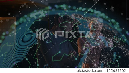 Examining network map, two tech professionals in business attire viewing holographic globe in lab 135083502