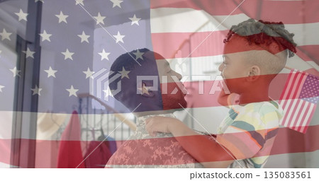 Service member in camouflage uniform holding son in striped t-shirt in hallway with American flag Service member in camouflage uniform holding son in striped t-shirt in hallway with American flag 135083561