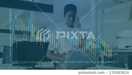 Working woman at desk using laptop in office interior, with monitor coffee cup and data graphs Working woman at desk using laptop in office interior, with monitor coffee cup and data graphs 135083624