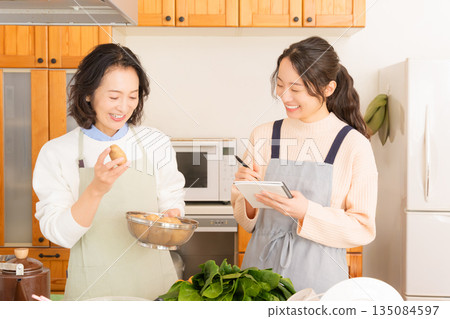 Daughter learning cooking from mother Daughter learning cooking from mother 135084597