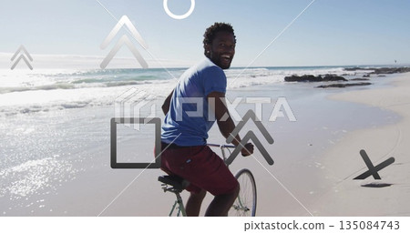 Cycling man in blue shirt red shorts looking back along wet sandy beach, with green bicycle Cycling man in blue shirt red shorts looking back along wet sandy beach, with green bicycle 135084743