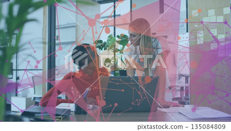 Collaborating office colleagues discussing project at office desk, with laptop and network overlay 135084809