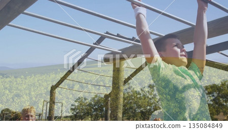 Climbing boy in green shirt gripping monkey bars at outdoor playground, with rope net, copy space Climbing boy in green shirt gripping monkey bars at outdoor playground, with rope net, copy space 135084849