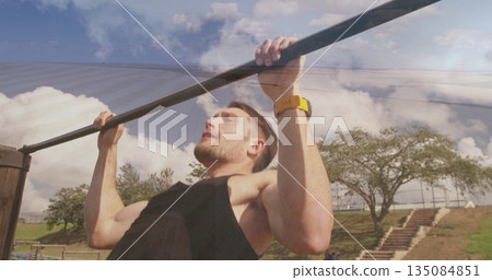 Muscular man in black tank top performing pull-up at park, with metal pull-up bar and smartwatch 135084851