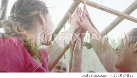 Stretching women raising arms and touching palms under monkey bars, wearing pink shirts and earbud 135084852