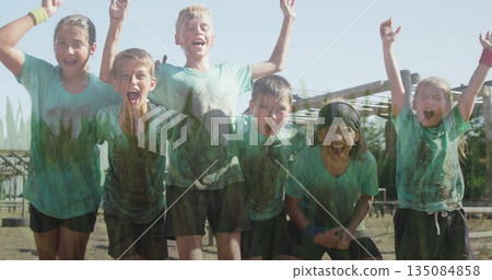 Cheering six kids covered in mud on course at camp, with headbands wristbands beams framework 135084858