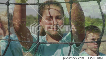 Gripping black rope net, girl and teammates standing on grass field in park, light blue shirts 135084861