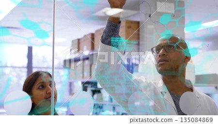 Collaborating scientists marking glass board at research lab, with turquoise digital graphics 135084869