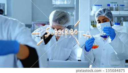 Lab techs in coats inspecting samples at microscope and pipetting blue and orange liquids in lab 135084875