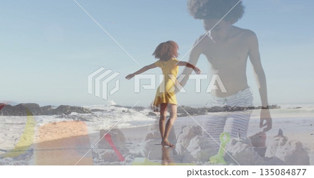 Twirling woman wearing yellow sundress balancing on sandy shore, with child sculpting sandcastle 135084877