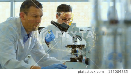 Scientists in lab coats examining slide under microscope at lab bench, with pipette data overlay 135084885