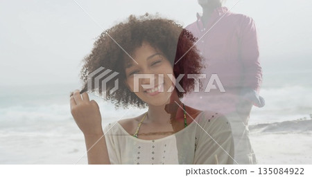 Smiling woman in summer top touching hair at sandy beach shoreline, with gentle waves, sea foam Smiling woman in summer top touching hair at sandy beach shoreline, with gentle waves, sea foam 135084922