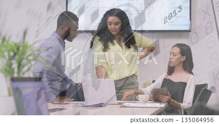 Pointing woman and colleagues analyzing charts at office meeting, with laptop tablet display screen 135084956