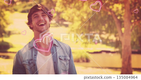 Laughing man in denim white tee in sunlit park by pond featuring pink hearts, copy space 135084964