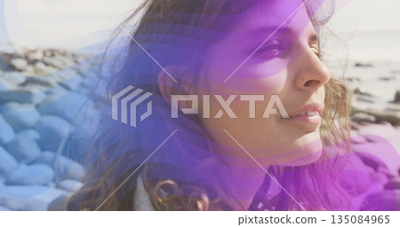 Standing profile woman wearing casual jacket facing calm sea on rocky shore, with rounded stones Standing profile woman wearing casual jacket facing calm sea on rocky shore, with rounded stones 135084965