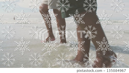 Walking father and son in swim trunks splashing waves in shallow ocean water on sandy seabed Walking father and son in swim trunks splashing waves in shallow ocean water on sandy seabed 135084967
