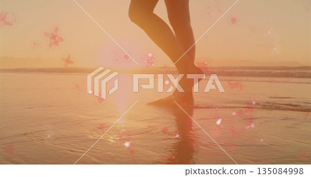 Wading woman's legs in swimwear across shallow water at sunset shore, with star-shaped flares 135084998