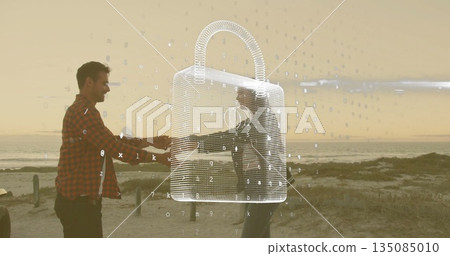 Shaking hands adults one wearing red-checkered shirt on beach at dusk, with padlock, fence posts Shaking hands adults one wearing red-checkered shirt on beach at dusk, with padlock, fence posts 135085010