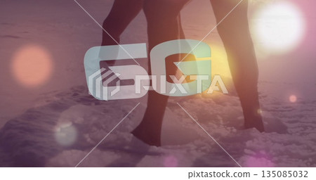 Standing couple wearing swimwear in shallow water on shore at sunset, with 5G overlay, lens flares 135085032