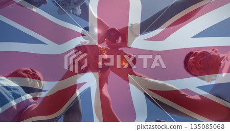 Raising group of five friends holding amber glass bottles under clear blue sky, Union Jack overlay 135085068