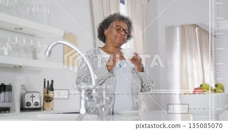 Holding white ceramic mug near lips woman in grey cardigan standing in kitchen, with steel faucet Holding white ceramic mug near lips woman in grey cardigan standing in kitchen, with steel faucet 135085070