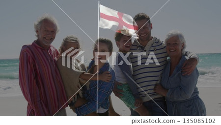 Standing three-generation family smiling at beach shoreline, holding white flag with red cross Standing three-generation family smiling at beach shoreline, holding white flag with red cross 135085102