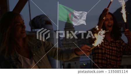 Waving two women holding sparklers on rooftop terrace at dusk, with Algerian flag fluttering Waving two women holding sparklers on rooftop terrace at dusk, with Algerian flag fluttering 135085114