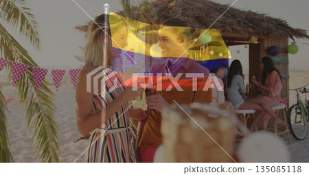 Woman in striped sundress and man in polo shirt chatting at beach bar with drinks, bunting Woman in striped sundress and man in polo shirt chatting at beach bar with drinks, bunting 135085118