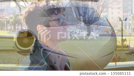 Showing man wearing sunglasses and coat merging private jet nose and turbofan engine at city park 135085131