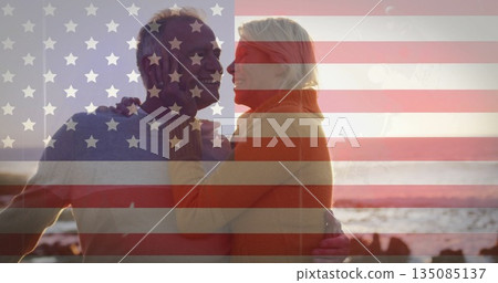 Embracing mature woman and senior man standing on rocky beach at sunset, wearing sweaters Embracing mature woman and senior man standing on rocky beach at sunset, wearing sweaters 135085137