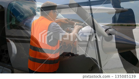 Man in high-vis vest checking engine through open cowling on apron, with crew observing propeller 135085139