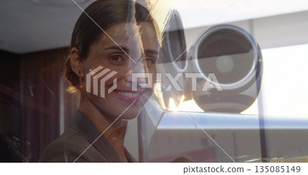 Standing professional in gray blazer examining lens device by wood wall in office, city reflections 135085149