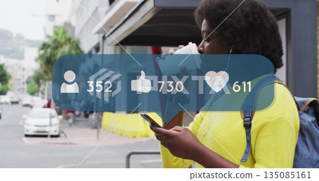 Holding coffee cup and scrolling smartphone on city sidewalk with earbuds and backpack, copy space 135085161