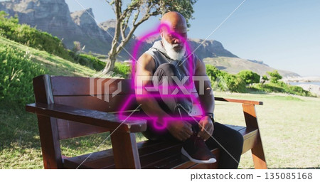 Tying shoelaces on running shoes African American man leaning on bench in grassy park, with earbuds 135085168