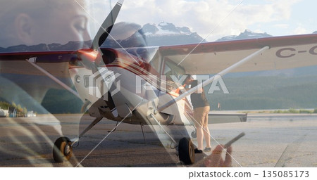 Leaning man inspecting single-engine plane on airstrip apron, with smartphone double-exposure 135085173