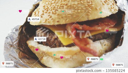 Bacon cheeseburger sitting in sesame-seed bun foil wrap on studio surface, with social media icons Bacon cheeseburger sitting in sesame-seed bun foil wrap on studio surface, with social media icons 135085224