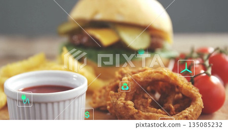 Displaying cheeseburger on dining table, beside French fries, onion rings, ketchup, cherry tomatoes 135085232