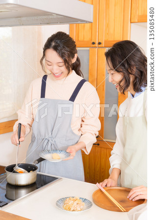 A mother tastes her daughter's meat and potato stew. 135085480