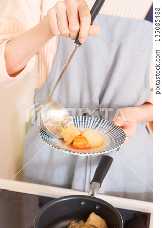 A young woman serving meat and potatoes on a plate 135085488