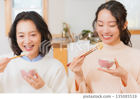 Mother and daughter eating together with hands together 135085519