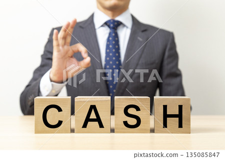 A businessman making an OK pose with a block that says "CASH" A businessman making an OK pose with a block that says "CASH" 135085847