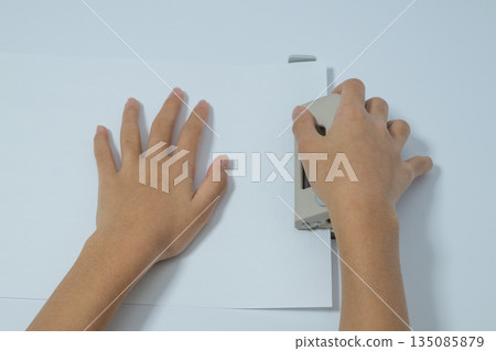從高空俯瞰,一個孩子正在紙上打孔。 從高空俯瞰,一個孩子正在紙上打孔。 135085879