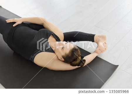 Reclined yoga stretch demonstrating deep flexibility and balance in serene studio Reclined yoga stretch demonstrating deep flexibility and balance in serene studio 135085966