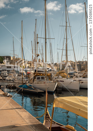 A picturesque view of Birgu Port filled with numerous boats, bathed in warm pre-sunset light. The tranquil waters reflect the golden hues, creating a serene maritime scene in Malta. 135086025