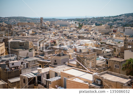 A breathtaking panoramic view of Gozo Island, showcasing its rolling hills, historic architecture, and stunning coastline under the Mediterranean sun. 135086032